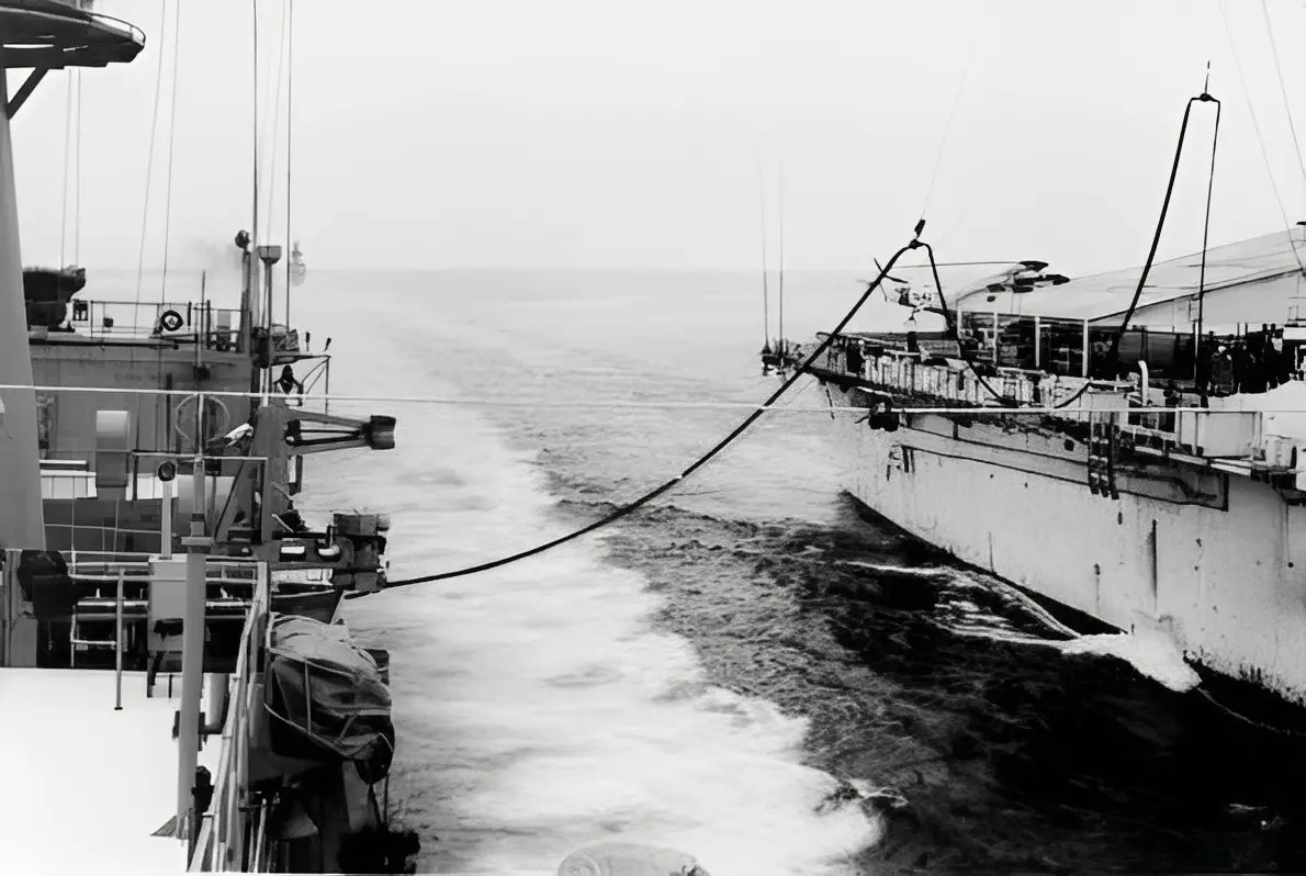 Two ships connected by fueling hose at sea.
