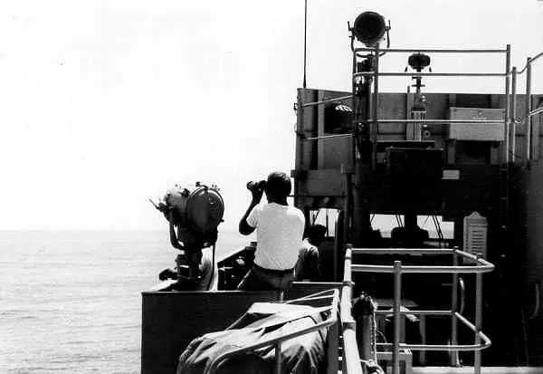 Person using binoculars on ship deck.